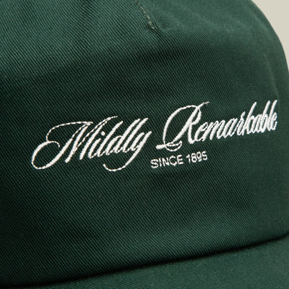 Close-up of the Goorin Bros. Mildly Remarkable Script dark green low pro fit cap featuring "Mildly Remarkable" and "SINCE 1895" embroidered in white script on the front, highlighting its classic embroidery.