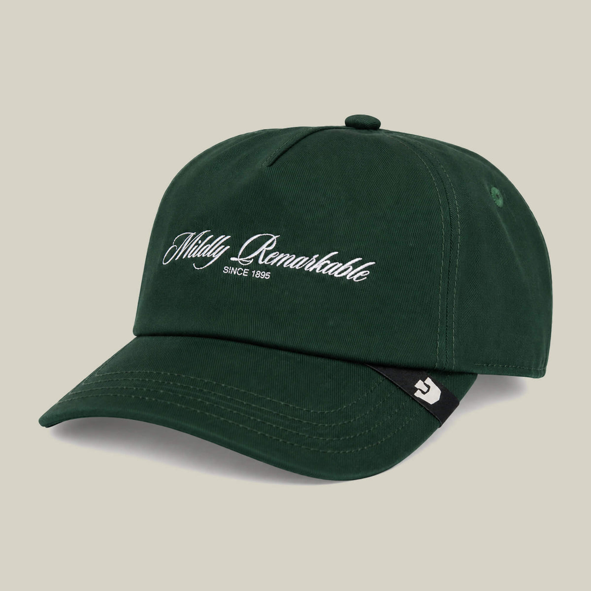 Goorin Bros. Mildly Remarkable Script cap in dark green, featuring "Mildly Remarkable" and "Since 1985" in white script on the front. A black tag with a white symbol accents the side of the brim for a subtle finish.