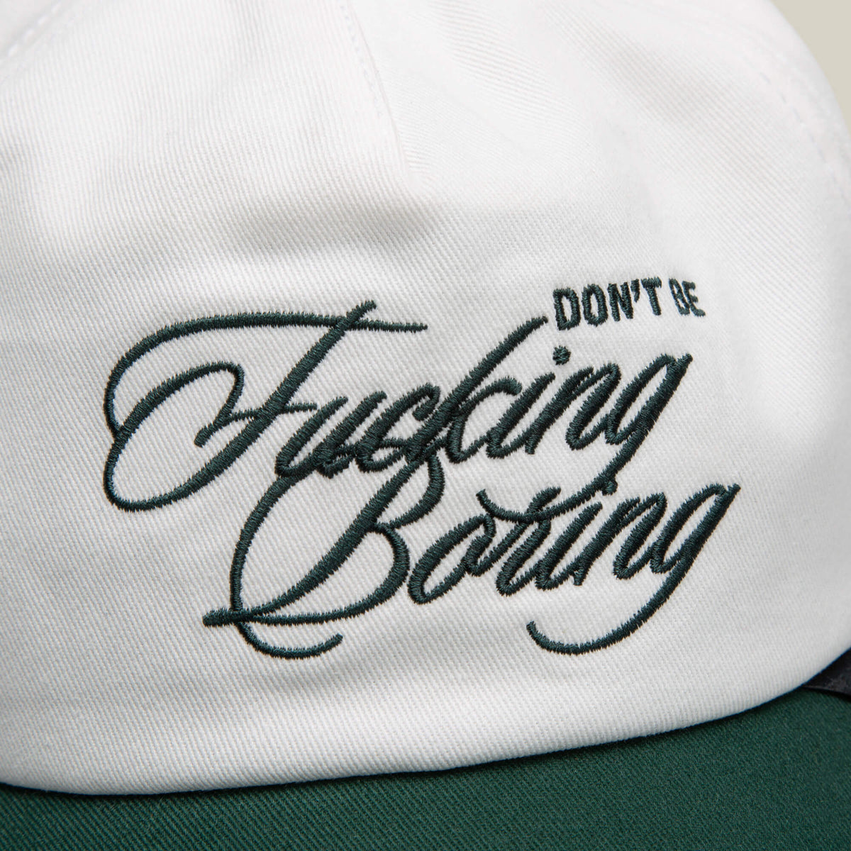 Close-up of a white two-tone Goorin Bros. cap featuring green embroidered text: "Don't Be Fucking Boring.