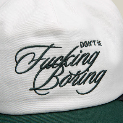 Close-up of a white two-tone Goorin Bros. cap featuring green embroidered text: "Don't Be Fucking Boring.