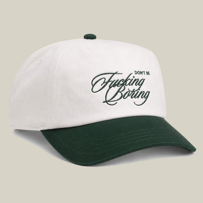 A white and dark green two-tone Goorin Bros. cap featuring "Don't Be Fucking Boring" embroidered in cursive on the front.