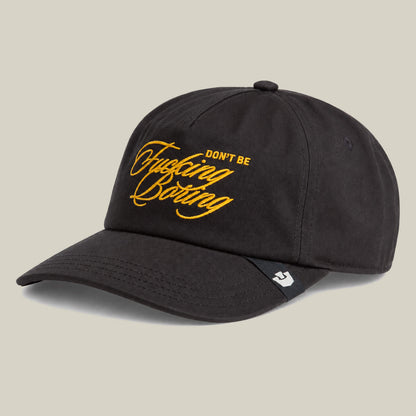 A black embroidered Goorin Bros. "Don't Be Fucking Boring" baseball cap with yellow text on the front is displayed against a plain beige background.