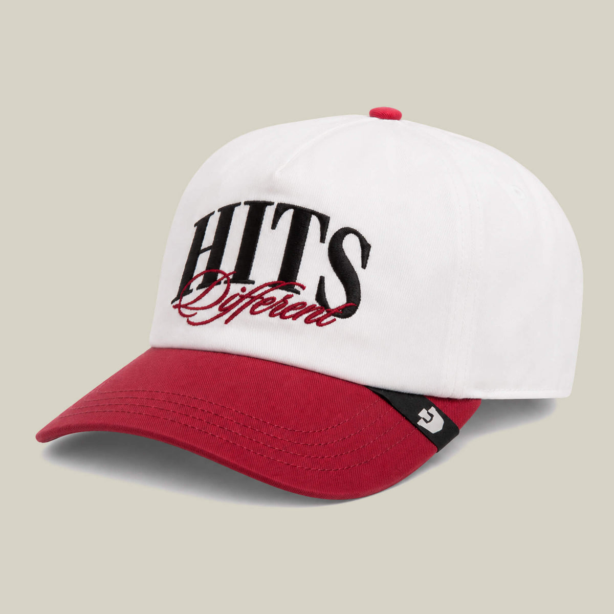 A white Goorin Bros. "Hits Different" baseball cap with a red curved brim and top button, featuring oversized embroidery of the phrase HITS Different on the front.