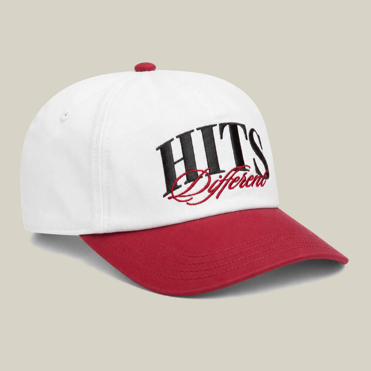 The Goorin Bros. Hits Different cap is white with a red curved brim and button, featuring "HITS Different" embroidered in black and red script on the front.