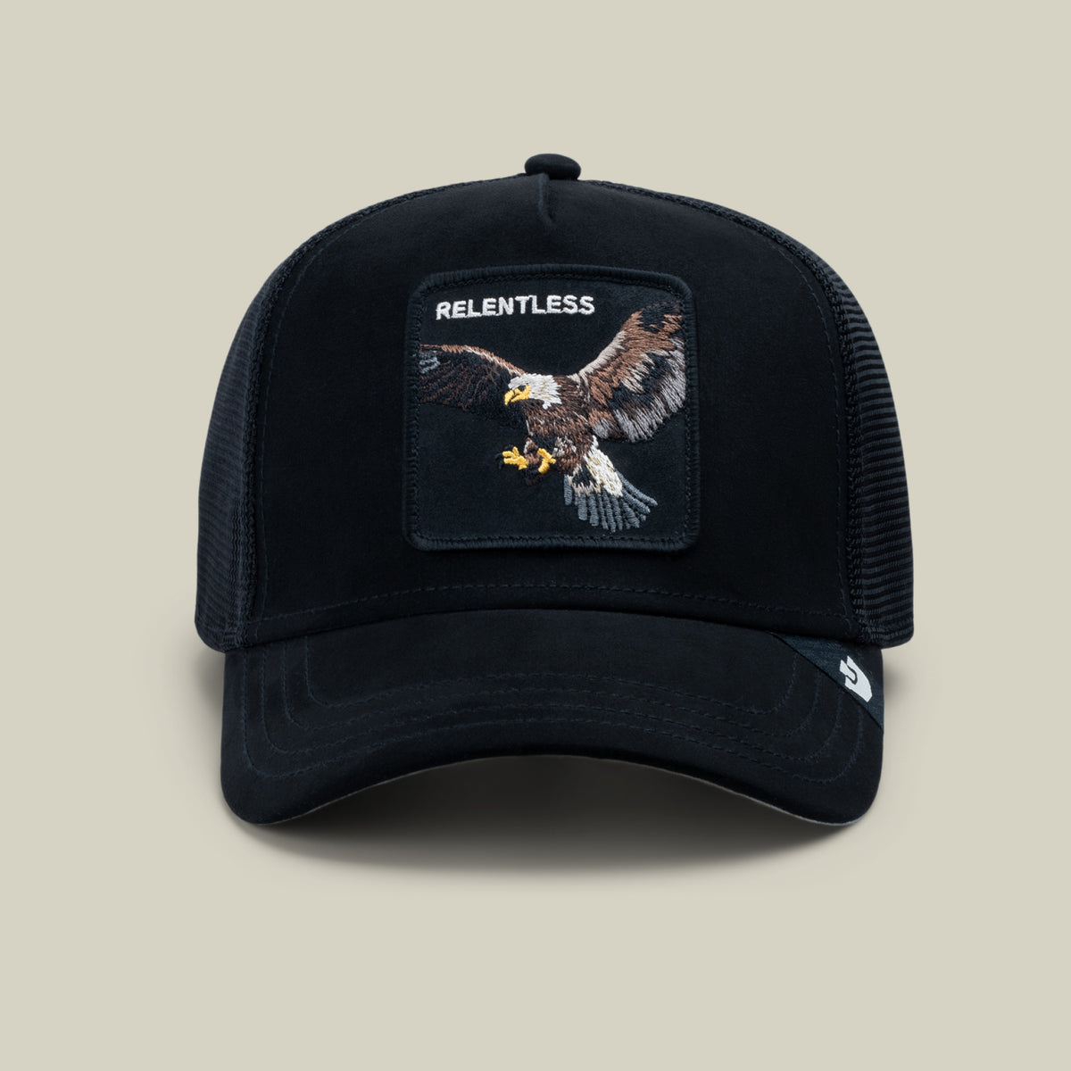 The Goorin Bros. Suede Relentless Eagle Trucker in Void features a black suede-feel brim, breathable mesh back, and a patch with an embroidered bald eagle topped by the word “RELENTLESS,” showcased against a plain light background.