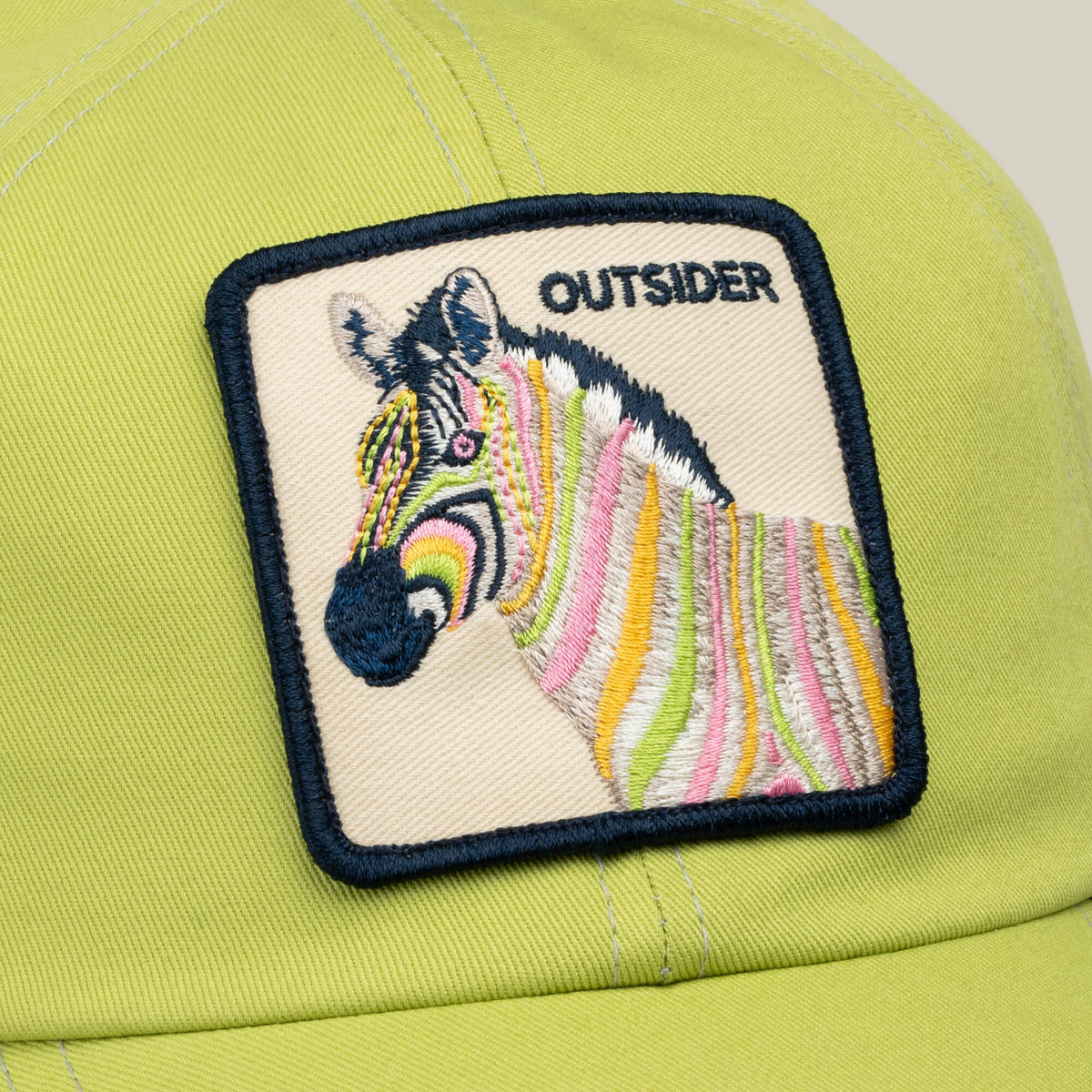 A yellow-green Goorin Bros. Outsiderland handmade baseball cap, featuring an embroidered patch with a colorful zebra and the word OUTSIDER in bold black text. Proudly made in the USA.