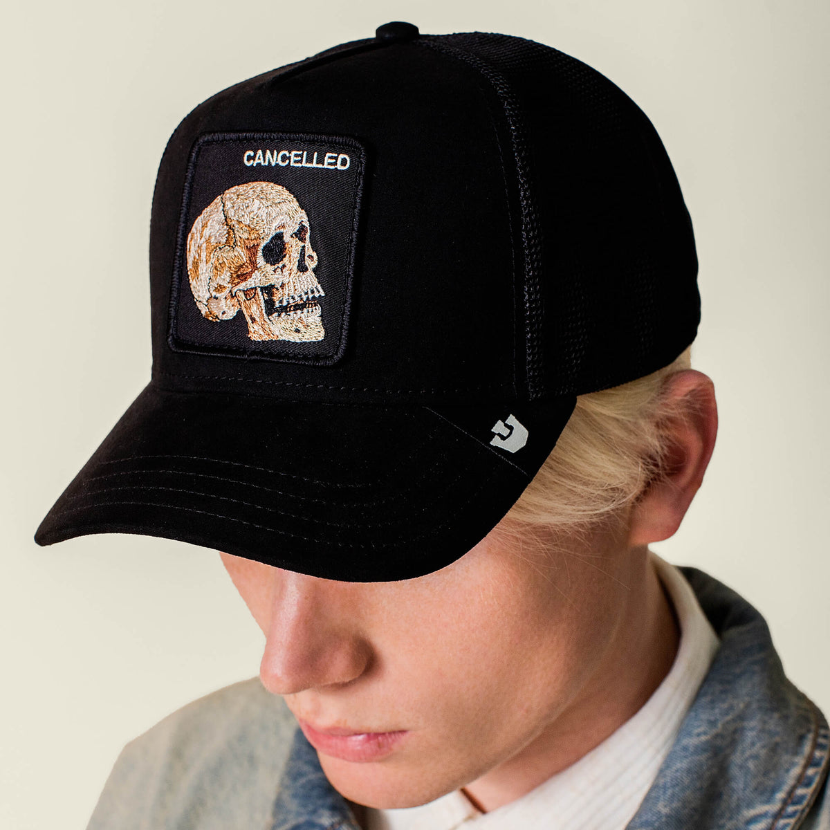 Wearing the Goorin Bros. Bold Suede Skull hat featuring a stitched skull and CANCELLED patch, paired with a light denim jacket, this person looks down.