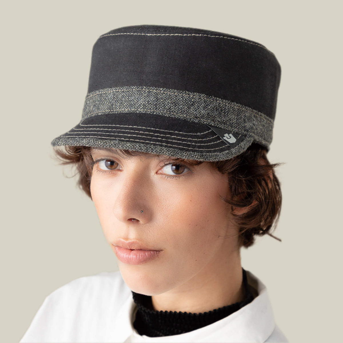 A person with short brown hair wears the Goorin Bros. Ampere black and gray striped flat-top cadet cap and a white collared shirt, looking at the camera against a neutral background.