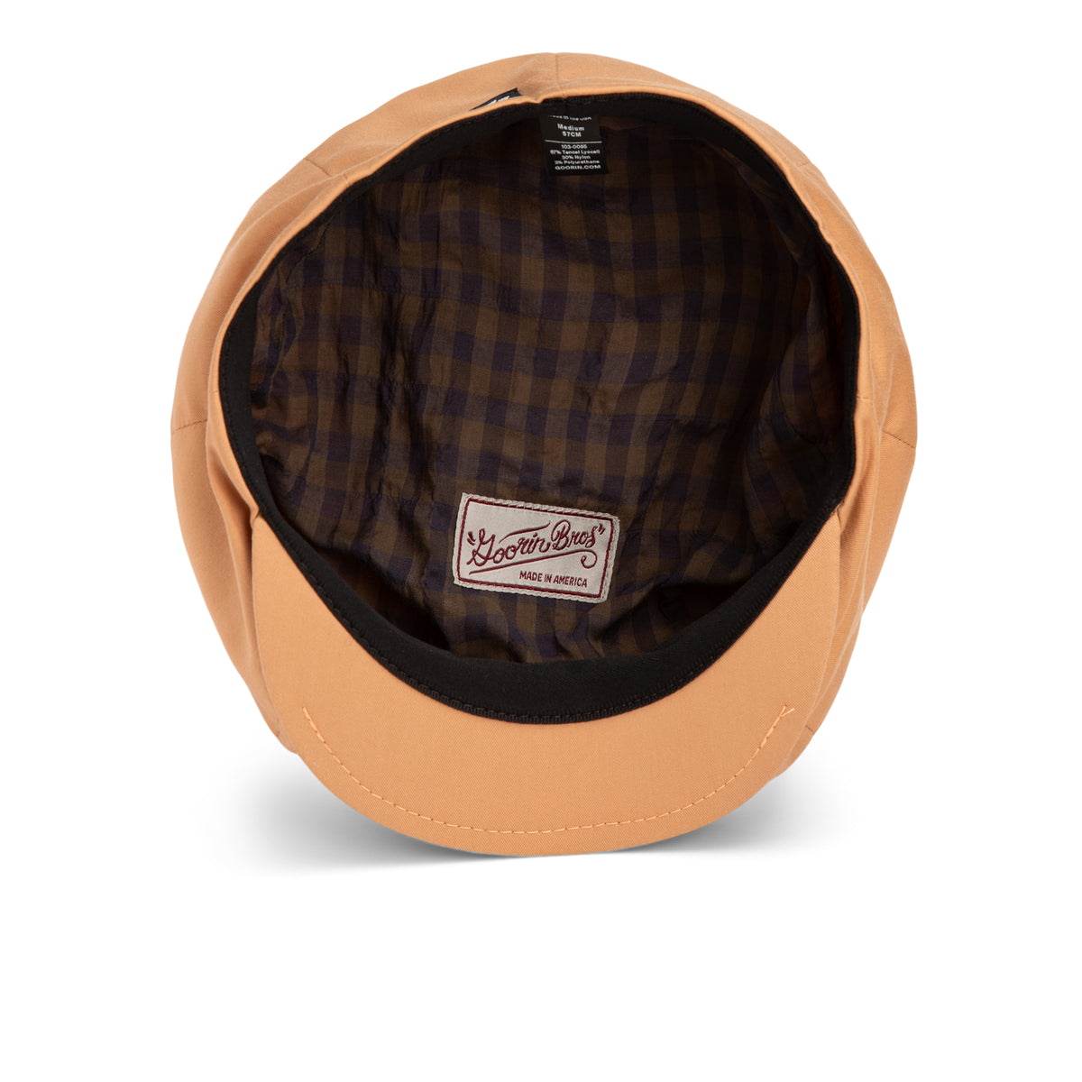 A tan cap viewed from above, showing a brown and navy checkered inner lining with a white label reading Goorin Bros. Chopping Block. Its unique shape and exclusive style give this piece an air of secret fashion sophistication.