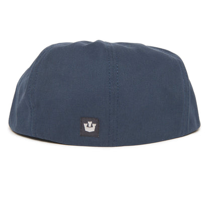 A navy blue cap shown from the back features a small black rectangular patch with a white crown emblem at the center bottom. The Goorin Bros. Mulberry Street flatcap draws inspiration from classic designs, blending timeless style with modern flair.