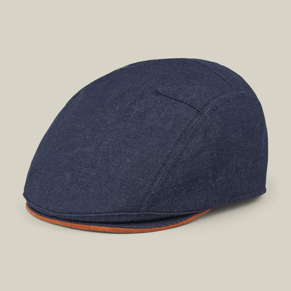 The Goorin Bros. Ashfield is a blue cotton suede flat cap with visible stitching and a brown-trimmed brim, made in the USA, shown against a plain light background.