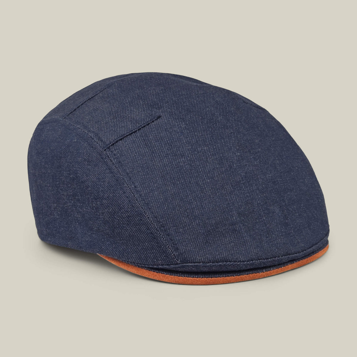 The Ashfield flat cap by Goorin Bros. features dark blue cotton suede with a subtle sheen and brown trim on the brim, made in the USA and shown on a plain light beige background.
