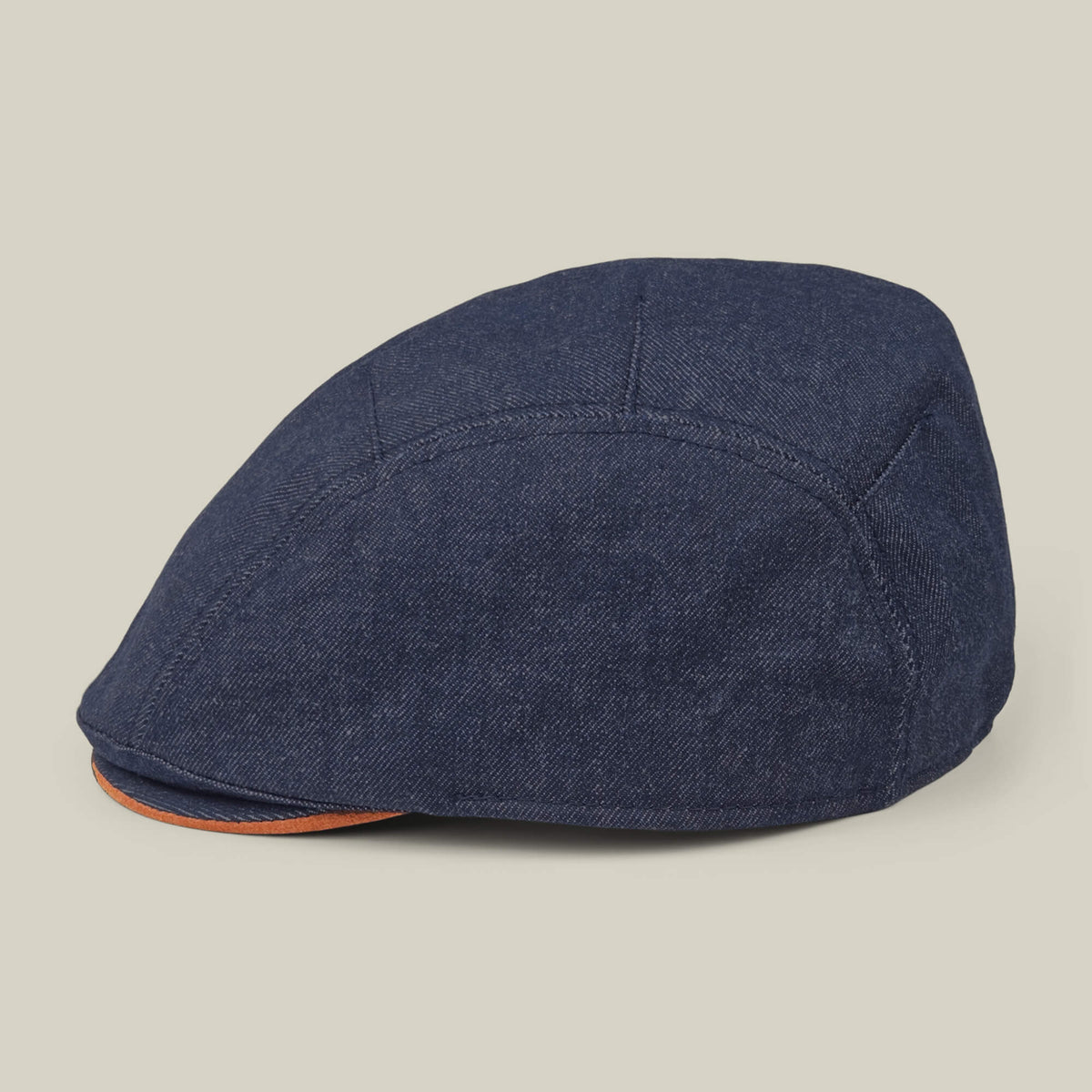 The Ashfield by Goorin Bros. is a dark blue cotton suede flat cap with visible stitching and an orange accent on the brim's edge, shown against a plain light background.