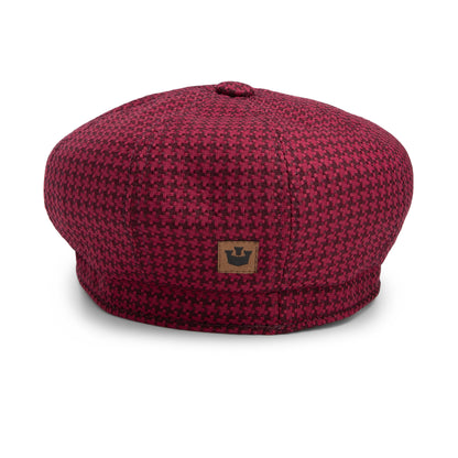 The Cold Snap by Goorin Bros. is a red and black houndstooth patterned beret, featuring a small brown patch with a black crown logo on the front and crafted with a German wicking sweatband for added comfort.