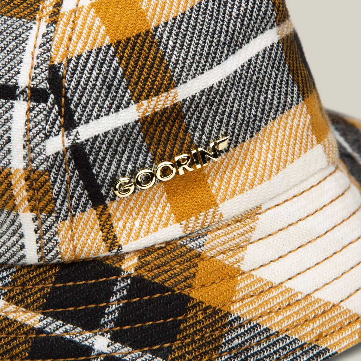 Close-up of the Bespoke Wordmark Bucket by Goorin Bros., featuring a yellow, black, and white plaid pattern with a metallic Goorin wordmark on cotton linen fabric.
