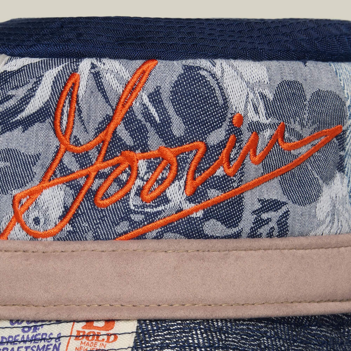 Close-up of the Goorin Bros. Goorin Rework Bucket: a navy and grey floral-patterned bucket hat featuring orange Goorin embroidery, beige trim, and crafted from recycled materials.