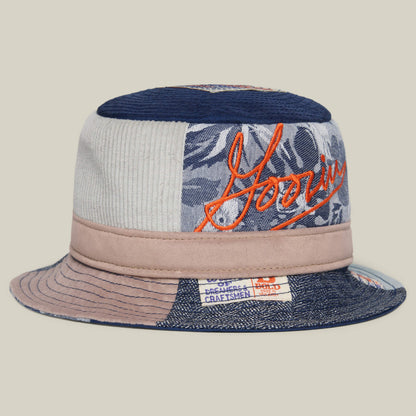 The Goorin Bros. Goorin Rework Bucket in EDGE features recycled materials, blue and beige patchwork, orange embroidery, and a Dreamers & Craftsmen label—an eco-friendly style for Earth Day.