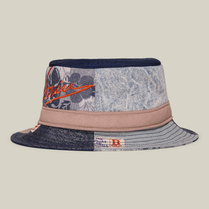 The Goorin Bros. Goorin Rework Bucket is a patchwork bucket hat with denim, floral, and striped patterns, tan accents, and red embroidered text, made in the USA.