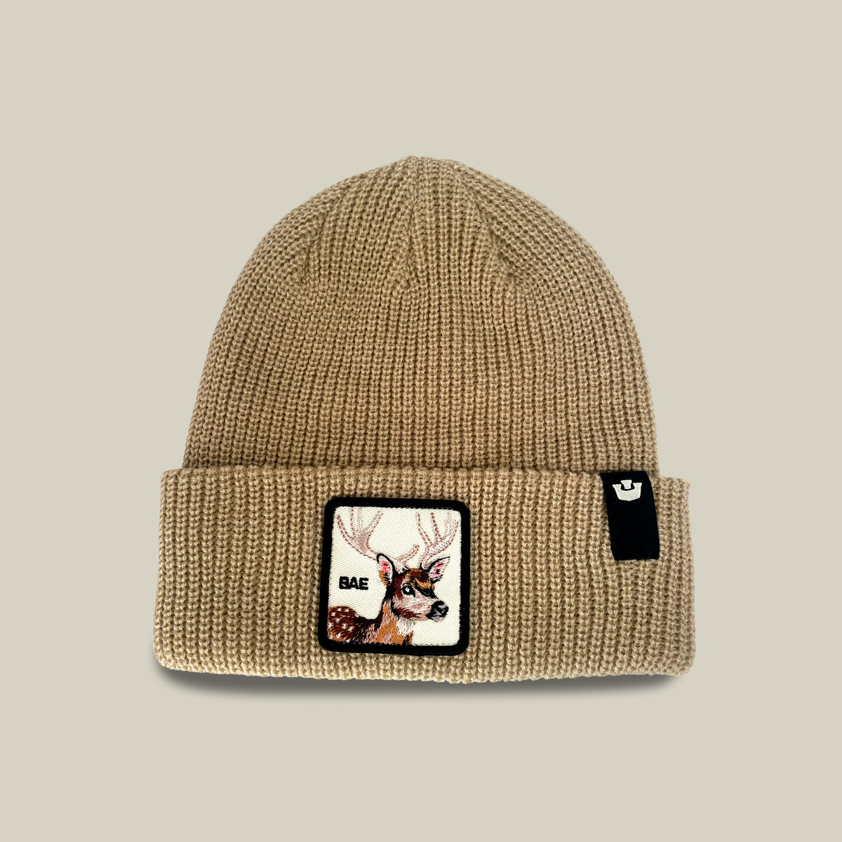 The Bae Beanie from Goorin Bros. is an everyday knit in a chalk hue, crafted from soft acrylic, and features a patch with a deer head and the word “BAE,” along with a small black tag on the cuff.