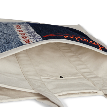 A close-up of the Goorin Bros. Goorin Reworked Tote highlights its interior lining, snap button closure, and a blue denim patch with red stitching and woven labels.