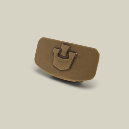 A stylish Castle CapLoc by Goorin Bros.—a small, rectangular, bronze-colored zinc alloy hat accessory featuring a raised geometric design on its front—is displayed on a plain light background.
