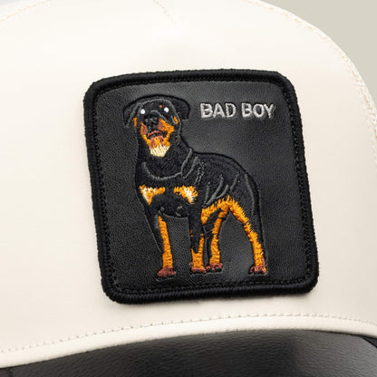A white and black faux leather trucker hat from Goorin Bros., called the Faux Leather Rottweiler, features a stitched patch of a Rottweiler with the words BAD BOY on the front.