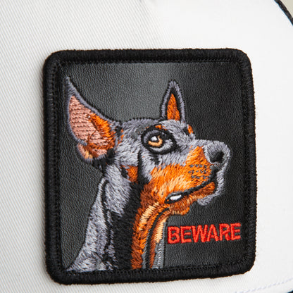 Add an eye-catching touch to your favorite accessory with the Goorin Bros. Beware Trucker Mini—a white fabric patch featuring an embroidered Doberman’s head and the word BEWARE stitched in red at the bottom right corner, perfect for customizing your hat or showing off some attitude.
