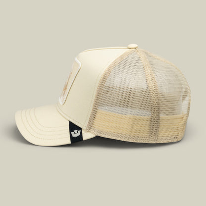 The Goorin Bros. Tonal Amigo Mini is a cream and beige two-tone trucker hat with a mesh back panel and small embroidered patch detail, shown in a side view against a neutral background.