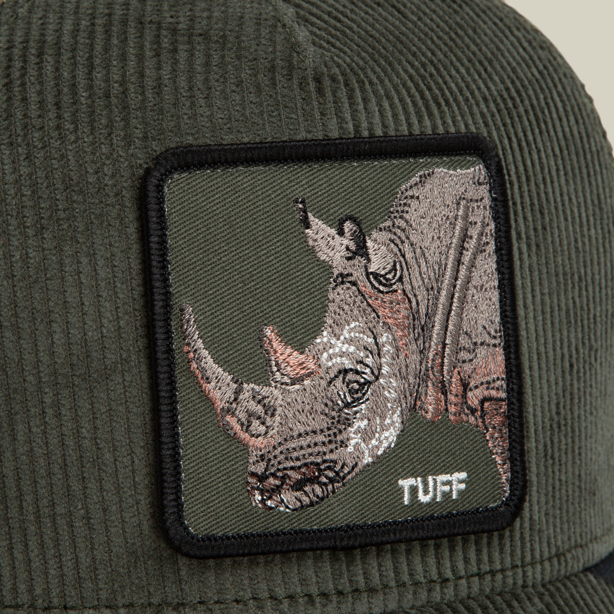 Close-up of the Goorin Bros. Corduroy Tuff hat—a green corduroy trucker cap crafted from a durable polyester-cotton blend, featuring a square embroidered patch with a rhinoceros and the word “TUFF” in white text.