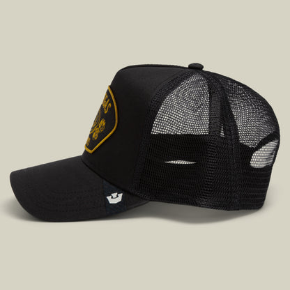 The Goorin Bros. Las Vegas trucker cap features black mesh construction with a curved brim and a bold yellow embroidered patch on the front. It also includes a small stitched label near the visor and is presented against a neutral background.