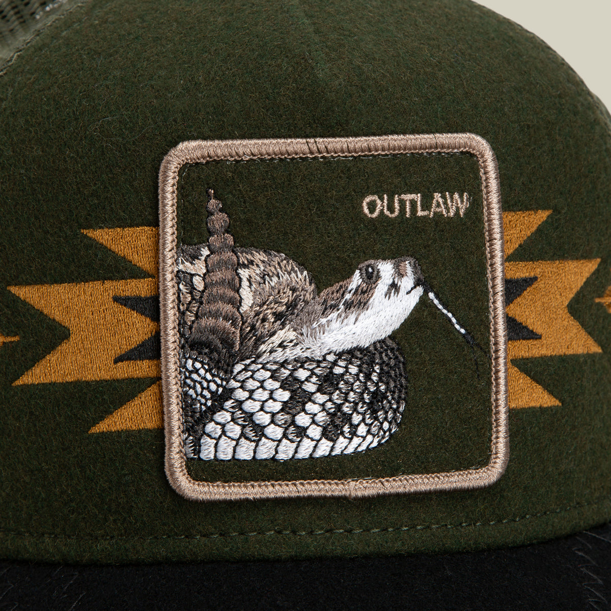 The Canyon Outlaw by Goorin Bros. is a dark green wool blend trucker hat, featuring a striking rattlesnake patch with the word OUTLAW. The patch’s tan border and bold yellow-orange geometric accents infuse the hat with unmistakable outlaw energy.