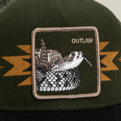 The Canyon Outlaw by Goorin Bros. is a dark green wool blend trucker hat, featuring a striking rattlesnake patch with the word OUTLAW. The patch’s tan border and bold yellow-orange geometric accents infuse the hat with unmistakable outlaw energy.