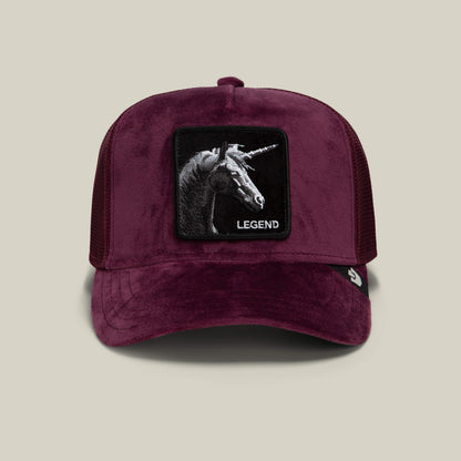 Goorin Bros. Velour Legend is a burgundy velour baseball cap in a classic trucker silhouette, featuring a mesh back and a striking patch with a black unicorn head and the word “LEGEND” embroidered beneath it.