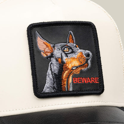 Close-up of the Goorin Bros. “Faux Leather Doberman” collectible hat, featuring a sewn patch with an embroidered dog and the word BEWARE in red letters on a white and black design.