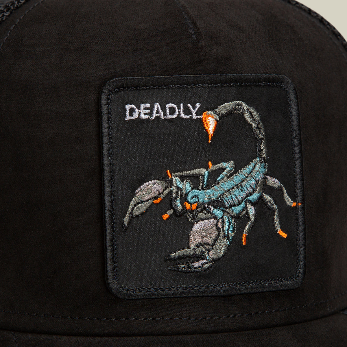 Close-up of the Suede Scorpion trucker hat by Goorin Bros., showcasing a black patch with an embroidered scorpion and the word DEADLY in white above it. The hat features breathable mesh panels for both comfort and style.