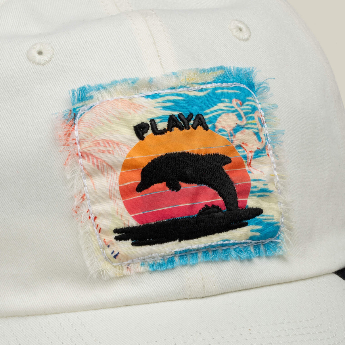 A white Goorin Bros. OOO Cap Fit hat features a sewn, distressed patch with a dolphin, sunset, and the word PLAYA embroidered in black, set against a blue sky and flamingos in the background—perfect for your Personal Beach Maintenance style.