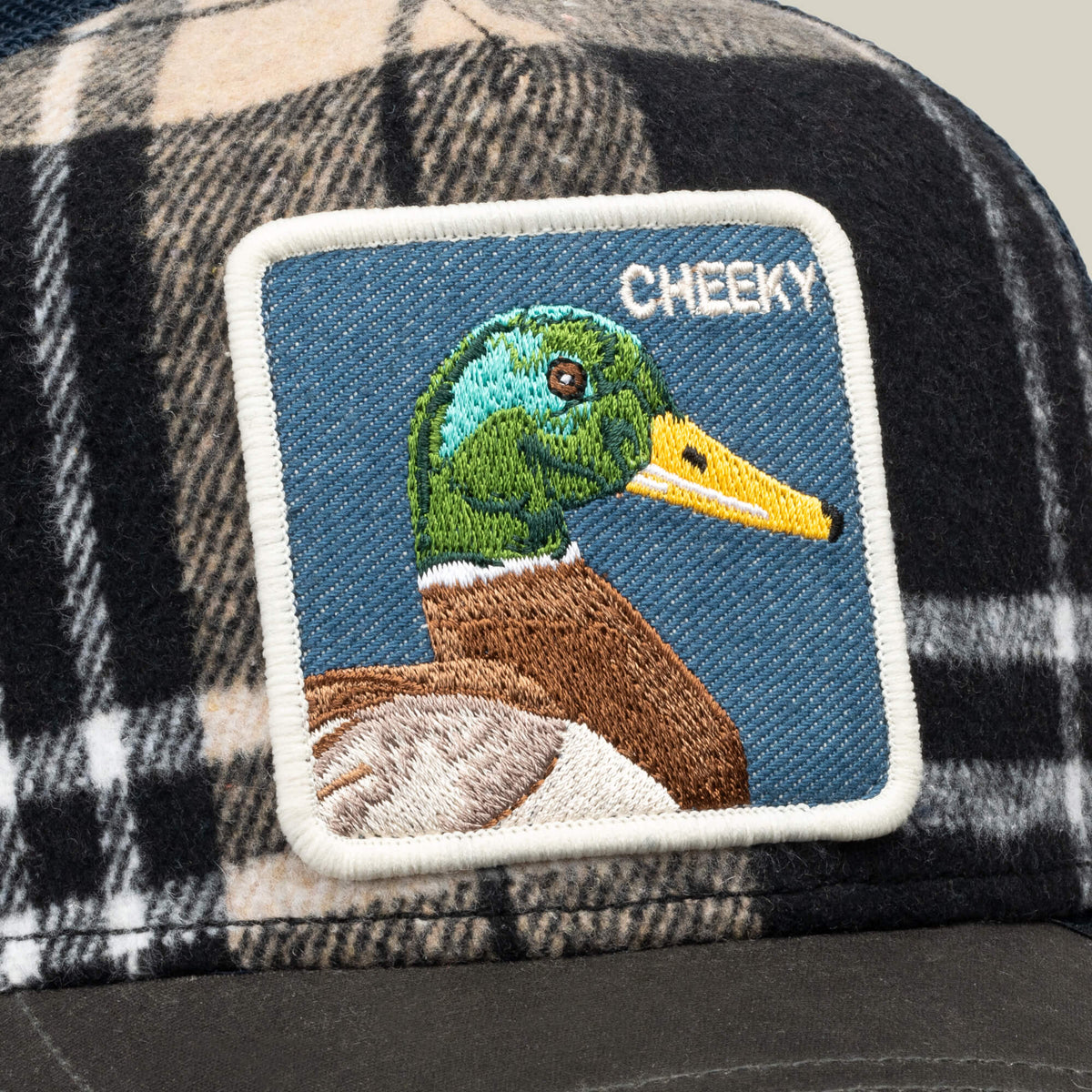 The Goorin Bros. Brit Cheeky cap is a plaid mesh hat with an embroidered patch showcasing a mallard duck and the word “CHEEKY” stitched in white on a blue background.