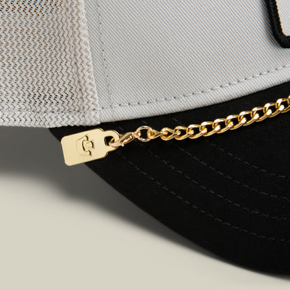 Close-up of a two-tone cap featuring the Goorin Bros. Mini CapLoc Chain—a striking piece of hat jewelry attached with a small metal tag—accented by a mesh back and black brim.