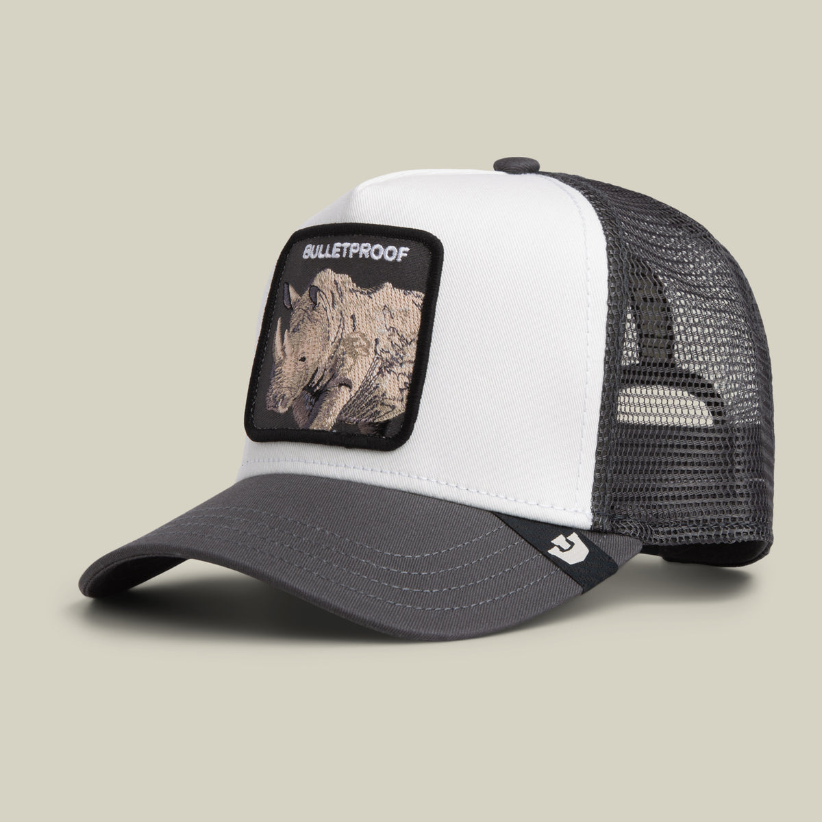 The Bulletproof Trucker by Goorin Bros. is a white and gray trucker hat featuring a black mesh back and a front embroidered patch with a rhino and the word “BULLETPROOF.”.