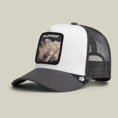 The Bulletproof Trucker by Goorin Bros. is a white and gray trucker hat featuring a black mesh back and a front embroidered patch with a rhino and the word “BULLETPROOF.”.