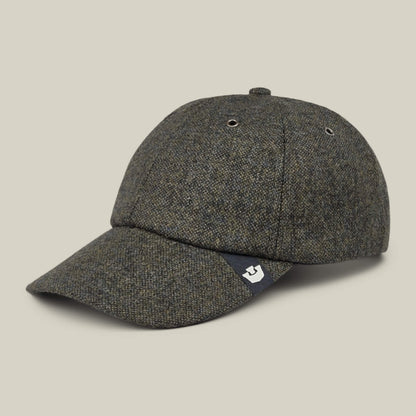 The Valmont by Goorin Bros. is a gray tweed wool baseball cap featuring a curved brim, two metal eyelets on each side, and a small black fabric tag with a white logo near the brim; proudly made in the USA.