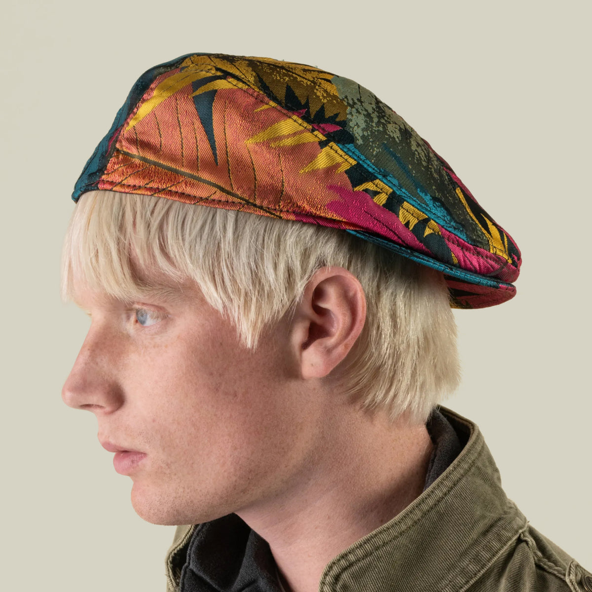 A person with light blonde hair wears the Upland Avenue, a colorful patterned beret by Goorin Bros., along with a green jacket, shown in profile against a plain background.