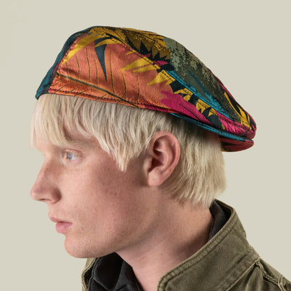 A person with light blonde hair wears the Upland Avenue, a colorful patterned beret by Goorin Bros., along with a green jacket, shown in profile against a plain background.