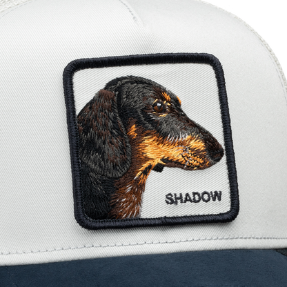 Here’s a rewritten sentence incorporating the provided product data: Close-up of the Goorin Bros. Suede Shadow trucker hat, featuring a suede brim and a stitched patch with a dachshund’s head in profile above the embroidered word “SHADOW.”.