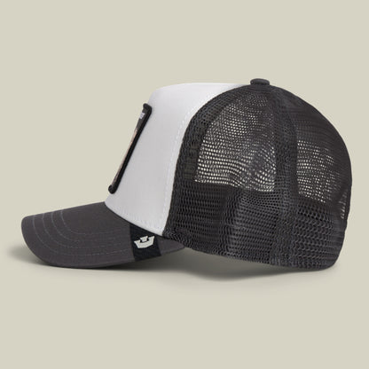 Side view of the Goorin Bros. Bulletproof Trucker hat, featuring a black and white mesh back design with a curved brim and a black embroidered patch on the front panel, displayed against a plain beige background.
