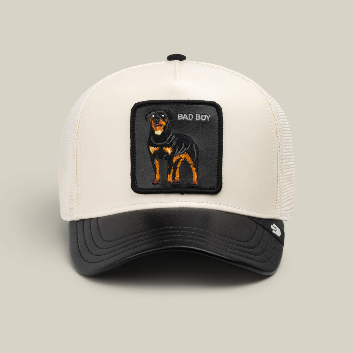 A white and black mesh trucker hat from Goorin Bros., named “Faux Leather Rottweiler,” featuring a bold patch of a Rottweiler and the words BAD BOY embroidered on the front.