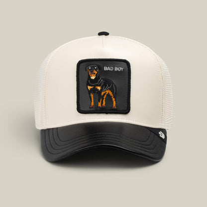 A white and black mesh trucker hat from Goorin Bros., named “Faux Leather Rottweiler,” featuring a bold patch of a Rottweiler and the words BAD BOY embroidered on the front.