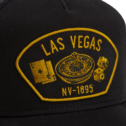 Black mesh-back trucker hat from Goorin Bros. featuring a yellow embroidered Las Vegas NV-1895 patch with playing cards, a roulette wheel, and dice—perfect for any Las Vegas enthusiast.