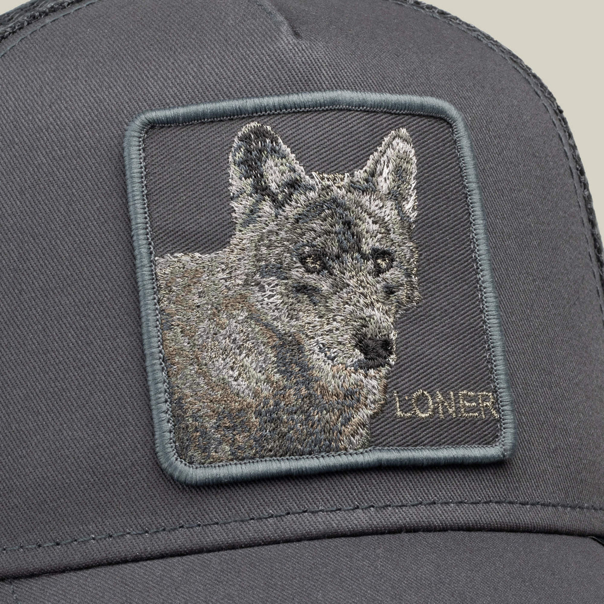 Close-up of the Goorin Bros. “Circle of Life - Loner” gray trucker cap, featuring an embroidered square patch with a wolf’s head and the word LONER stitched in the bottom right corner.