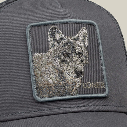 Close-up of the Goorin Bros. “Circle of Life - Loner” gray trucker cap, featuring an embroidered square patch with a wolf’s head and the word LONER stitched in the bottom right corner.